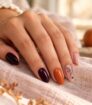 Manicura Halloween en tonos nude, naranja y ciruela con una delicada telaraña negra.